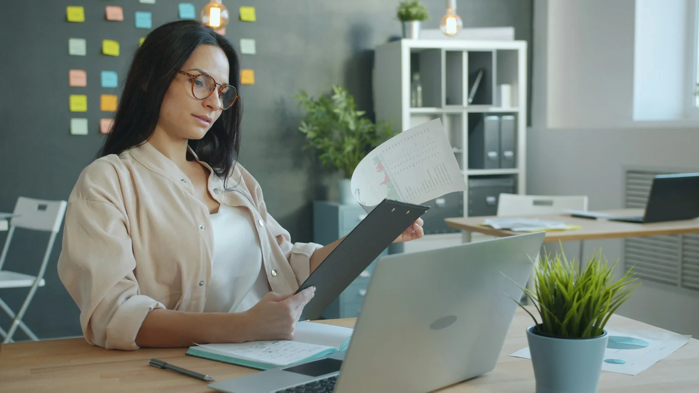 Une employée consulte un document sur un support à pince devant son ordinateur