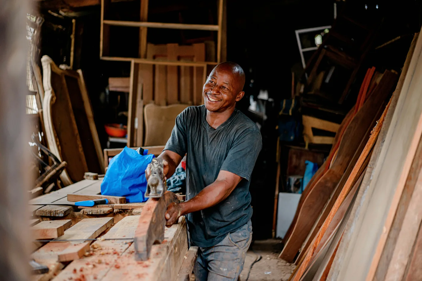 Artisan souriant qui travaille une planche de bois dans son atelier de menuiserie