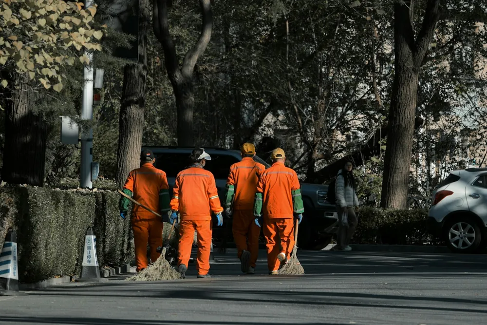 Agents en tenue orange marchant dans une rue avec des balais