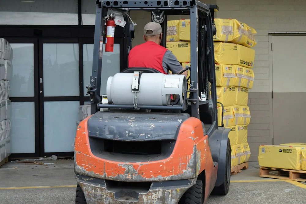 Chariot élévateur orange chargé de sacs jaunes dans un entrepôt