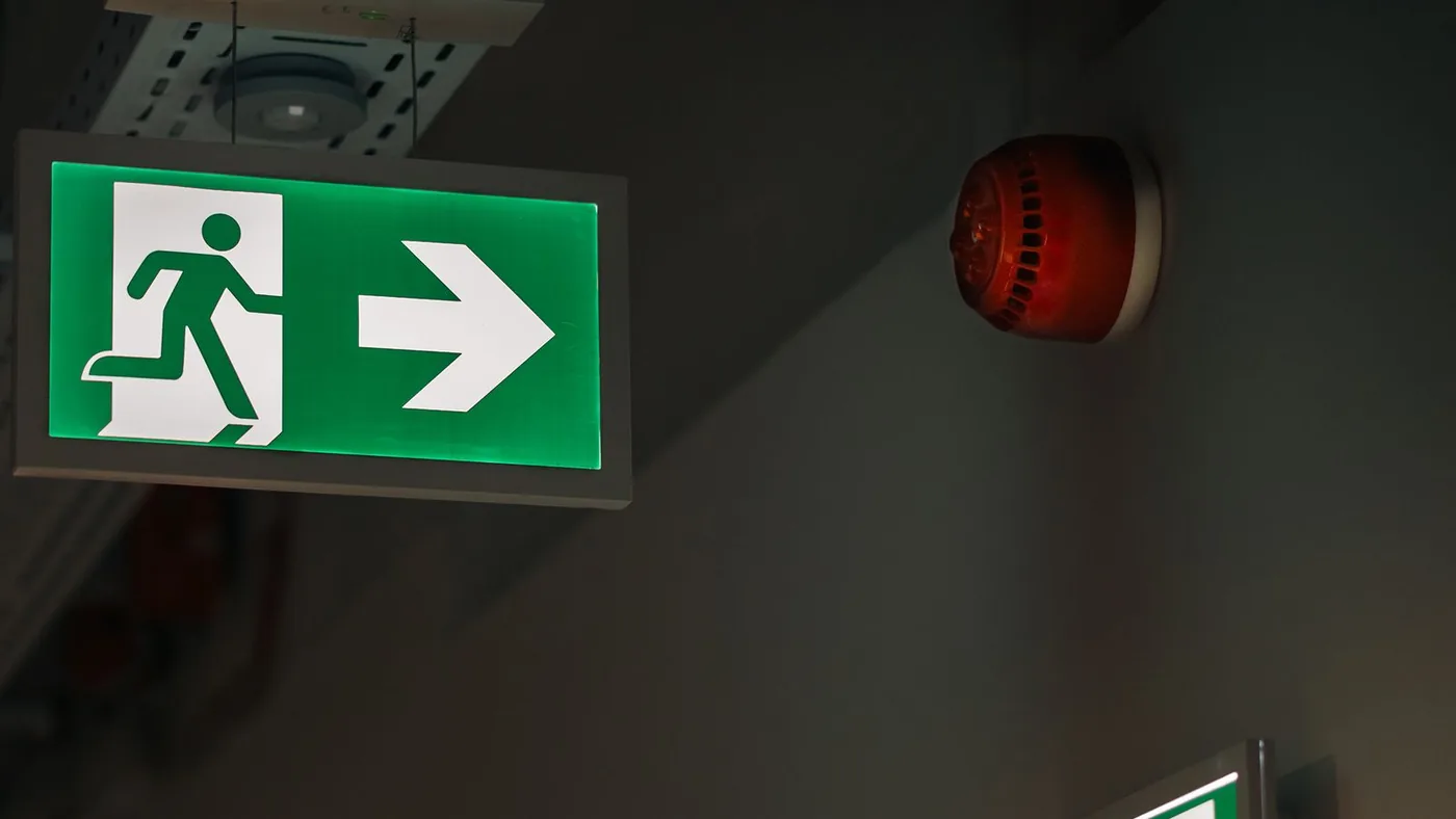 Un panneau de sortie de secours vert et une alarme sonore rouge sous un plafond